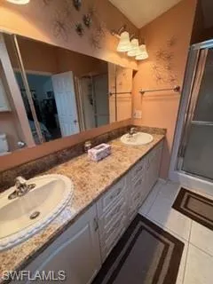 Full bath featuring double vanity, light tile patterned flooring, and a stall shower
