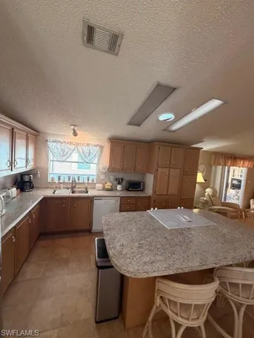 Kitchen featuring a kitchen bar, a textured ceiling, dishwasher, light stone countertops, and open floor plan