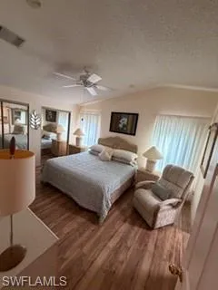 Bedroom featuring wood finished floors, lofted ceiling, a textured ceiling, a ceiling fan, and a closet