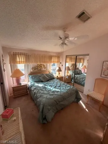 Bedroom with carpet floors, a textured ceiling, multiple windows, lofted ceiling, and a closet