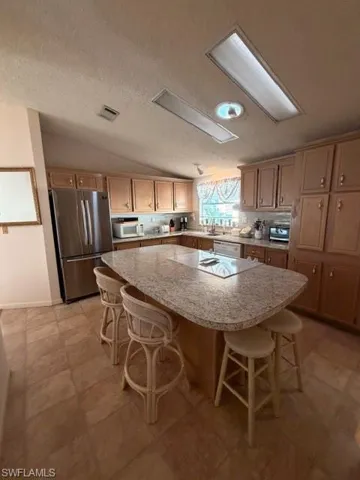 Kitchen featuring a kitchen island, a kitchen bar, fridge, lofted ceiling, and a textured ceiling