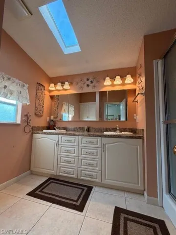 Full bath featuring double vanity, a textured ceiling, a skylight, a shower with shower door, and light tile patterned flooring