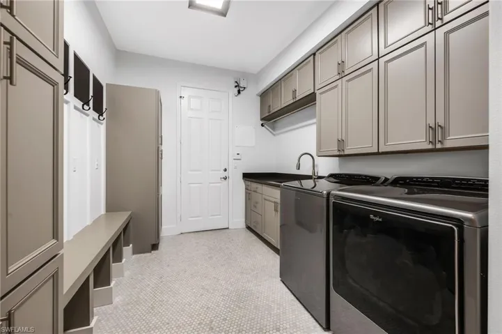Spacious utility room featuring extensive built-in cabinetry, durable hexagon tile flooring, a utility sink, and a built-in bench with storage