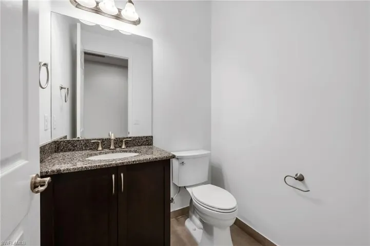 Powder room featuring a dark wood-finish vanity with a granite countertop, undermount sink, and brushed nickel fixtures