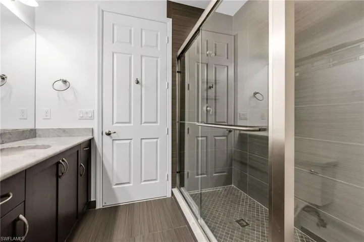 Modern bathroom featuring a frameless glass shower enclosure with horizontal gray tilework and diamond-patterned floor tiling