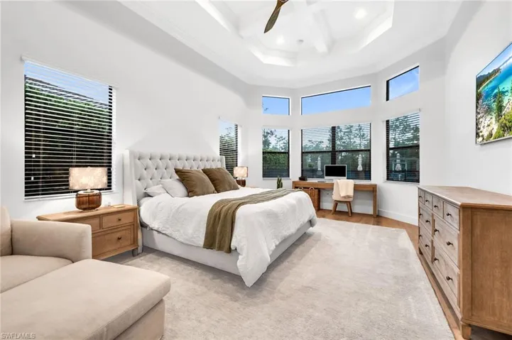 Spacious room featuring a tray ceiling with a fan, a bay window with high transom windows, and wood-finish flooring