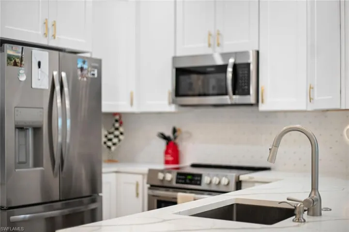 Kitchen featuring stainless steel appliances, white cabinetry, light stone countertops, and backsplash