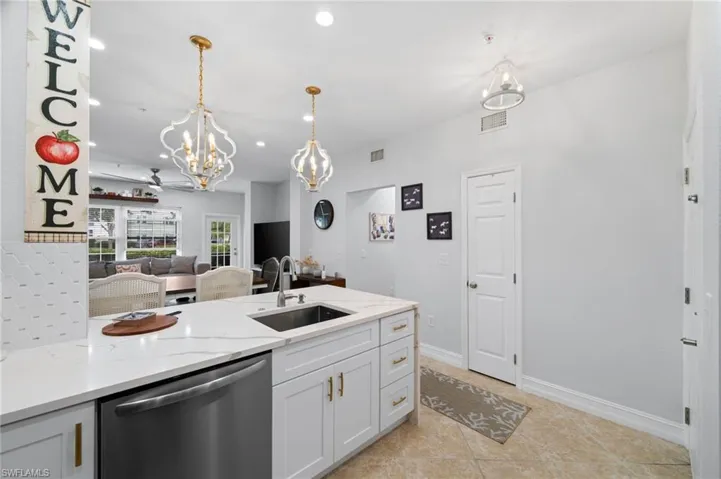 Kitchen with dishwasher, hanging lights, light stone counters, white cabinets, and light tile patterned flooring