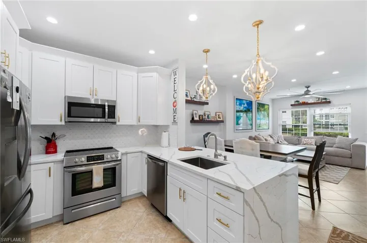Kitchen with stainless steel appliances, a chandelier, a peninsula, light stone counters, and decorative backsplash