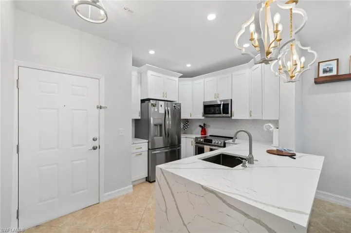 Kitchen featuring light stone countertops, a peninsula, white cabinets, stainless steel appliances, and a chandelier