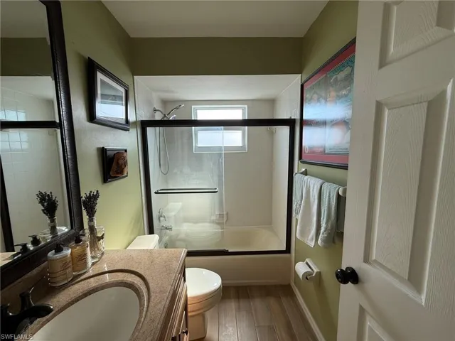 Full bathroom with toilet, wood finished floors, vanity, enclosed tub / shower combo, and baseboards