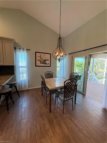 Dining space featuring plenty of natural light, a notable chandelier, high vaulted ceiling, and dark wood-type flooring