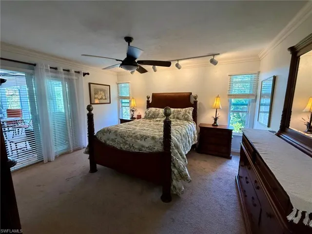 Carpeted bedroom with a ceiling fan, multiple windows, and crown molding
