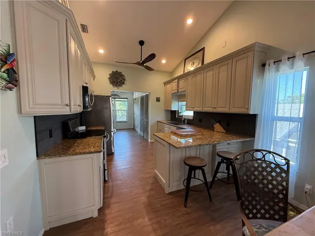 Kitchen with visible vents, a sink, ceiling fan, stainless steel microwave, and a kitchen breakfast bar