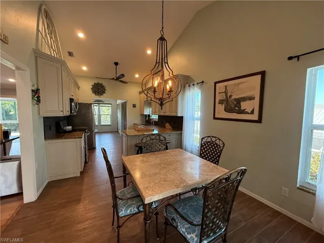 Dining space featuring ceiling fan with notable chandelier, high vaulted ceiling, visible vents, recessed lighting, and dark wood-style flooring