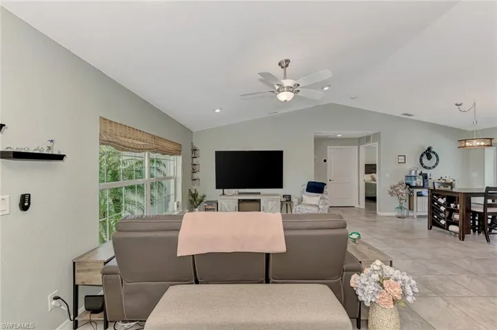 Living room with light tile patterned floors, lofted ceiling, and ceiling fan