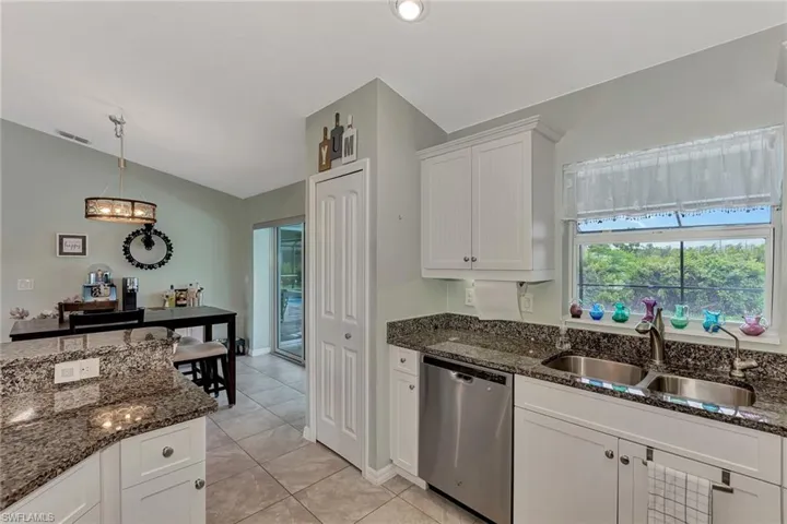 Kitchen with dark stone counters, white cabinets, sink, stainless steel dishwasher, and light tile patterned flooring