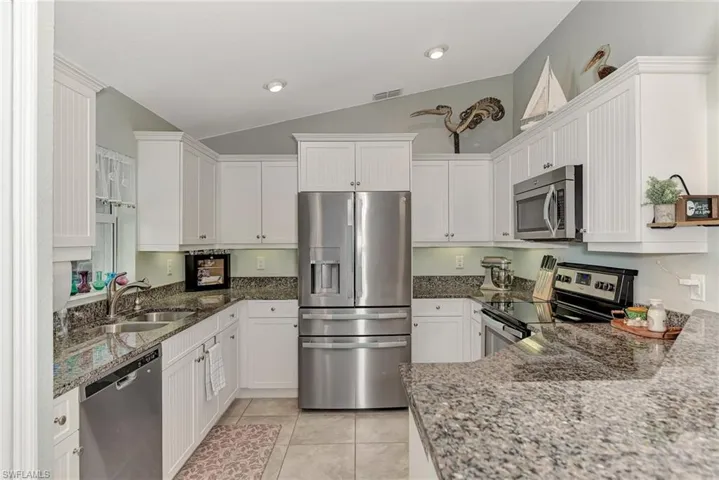 Kitchen with appliances with stainless steel finishes, light stone counters, vaulted ceiling, and white cabinetry