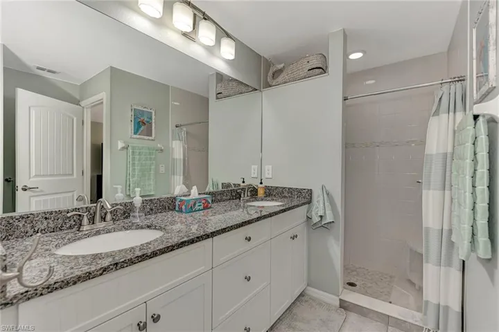 Bathroom with a shower with curtain, tile patterned floors, and dual bowl vanity
