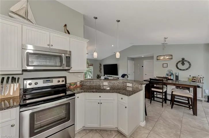 Kitchen with dark stone counters, white cabinetry, decorative light fixtures, appliances with stainless steel finishes, and lofted ceiling