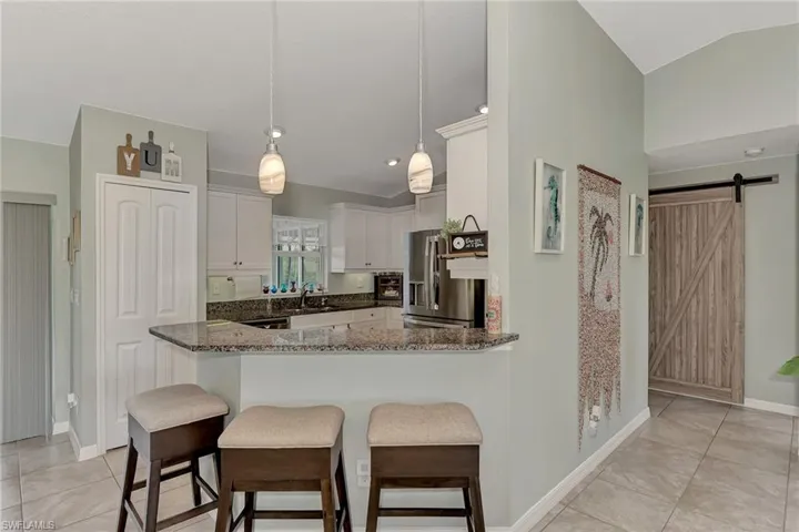 Kitchen featuring white cabinets, pendant lighting, a barn door, stainless steel fridge with ice dispenser, and dark stone countertops