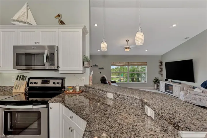 Kitchen with stainless steel appliances, kitchen peninsula, stone countertops, white cabinetry, and ceiling fan