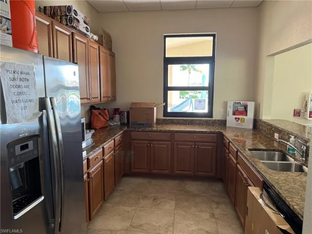 Clubhouse kitchen with dark stone counters, dishwashing machine, light tile floors, sink, and stainless steel fridge with ice dispenser