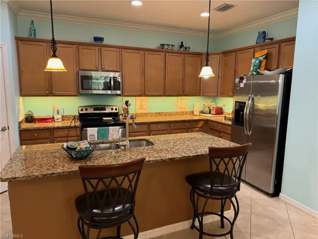 Kitchen with pendant lighting, appliances with stainless steel finishes, light tile floors, and a kitchen island with sink