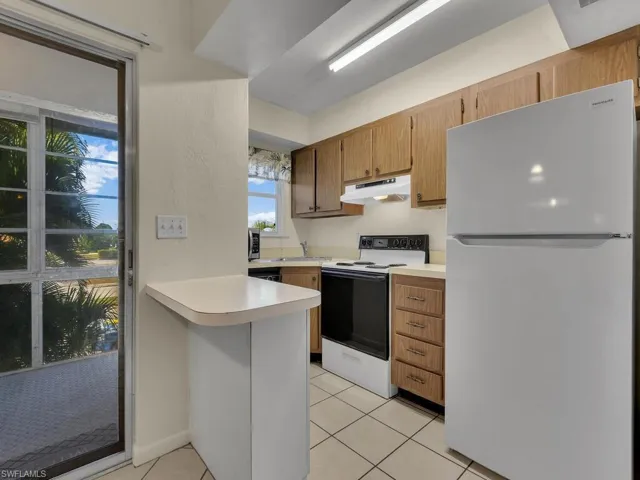 Kitchen with white appliances, light countertops, a peninsula, under cabinet range hood, and light tile patterned floors