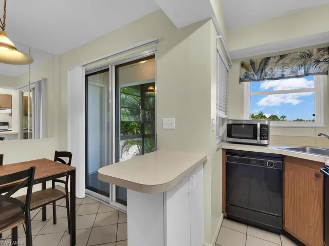 Kitchen featuring dishwasher, light countertops, stainless steel microwave, decorative light fixtures, and light tile patterned floors