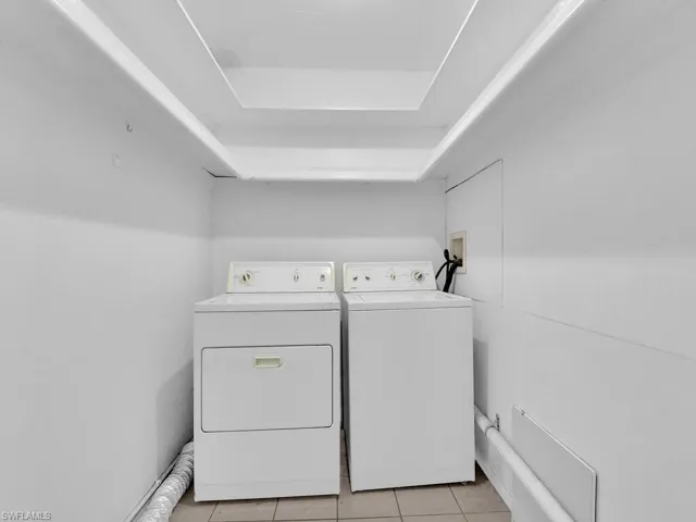 Washroom with light tile patterned flooring, a tray ceiling, and separate washer and dryer