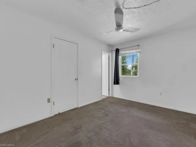Unfurnished bedroom with a textured ceiling, dark carpet, and ceiling fan