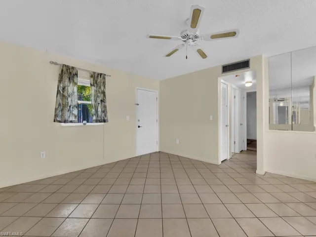 Tiled empty room with ceiling fan and a textured ceiling