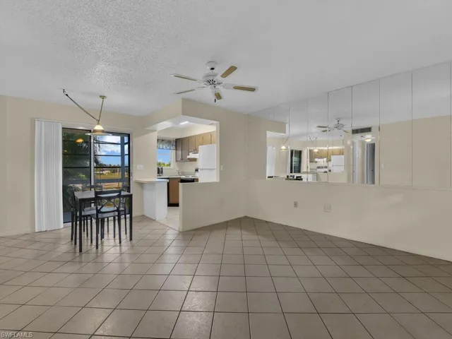 Living room with ceiling fan, a textured ceiling, and light tile patterned floors