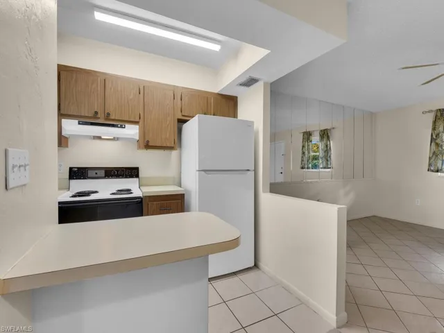 Kitchen with light countertops, range with electric cooktop, freestanding refrigerator, a peninsula, and under cabinet range hood
