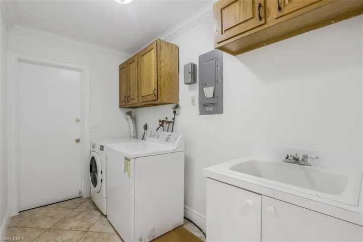 Laundry room with cabinets, electric panel, washer and dryer, light tile patterned floors, and ornamental molding