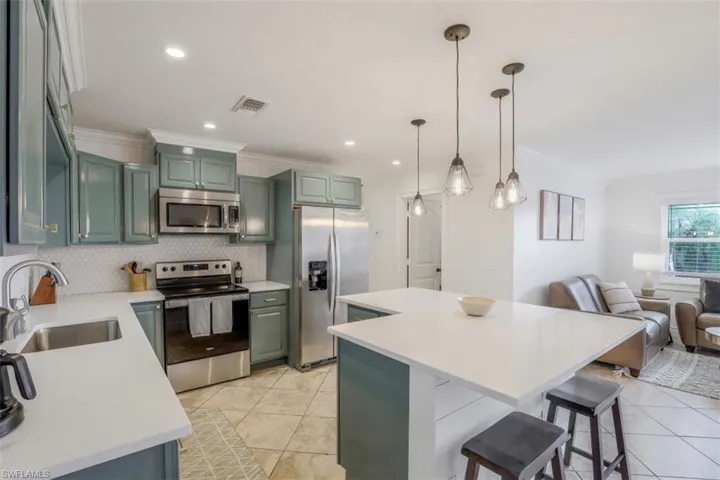 Kitchen featuring appliances with stainless steel finishes, pendant lighting, a center island, ornamental molding, and sink