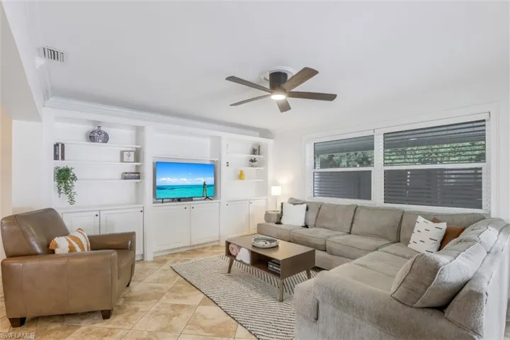 Living room with light tile patterned floors, built in shelves, ornamental molding, and ceiling fan