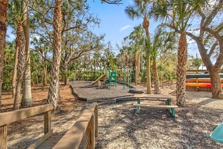Outdoor recreational area featuring a playground with a slide, a picnic table, and abundant palm trees