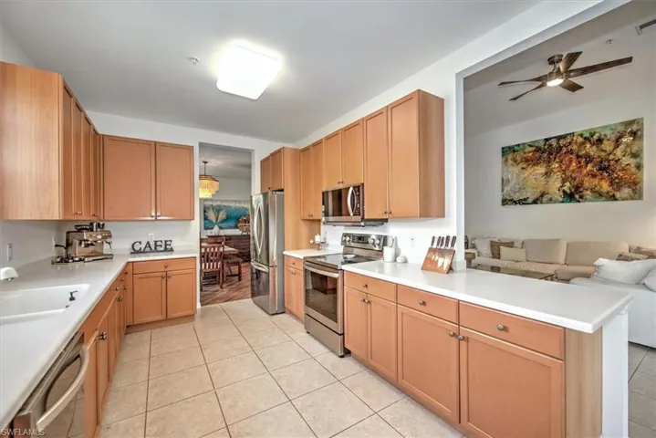 Kitchen with L-shaped light wood-finish cabinetry, light-toned countertops, stainless steel appliances, and tile flooring