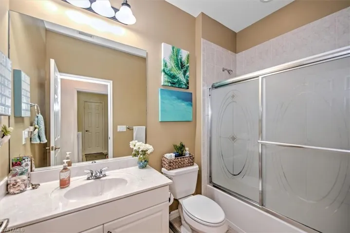 Bathroom featuring a single vanity with an integrated sink and light-toned countertop, a full-width mirror, and a combination tub/shower with frosted glass sliding doors