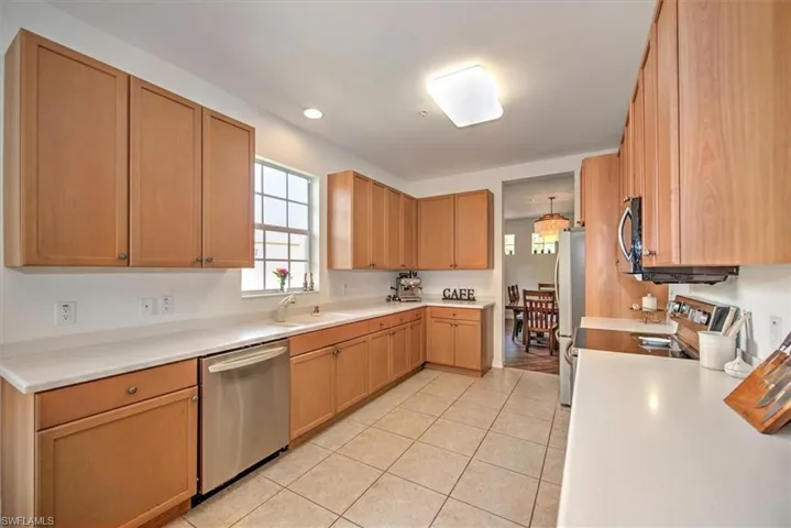 Kitchen featuring light wood-finish cabinetry, white countertops, tile flooring, and a stainless steel dishwasher