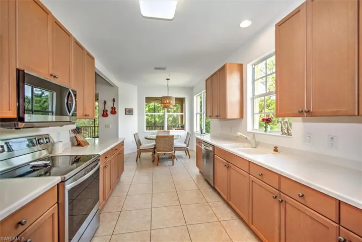 Kitchen featuring light wood cabinetry, light-toned countertops, tile flooring, and stainless steel appliances including a microwave and range