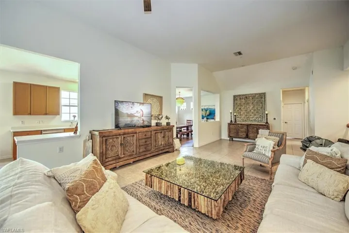 Spacious living area featuring vaulted ceilings, tile flooring, and a kitchen pass-through with a built-in countertop