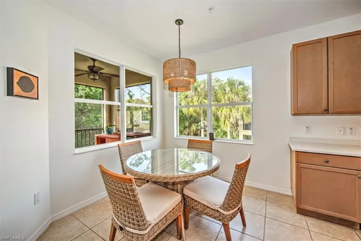 Bright dining area featuring multiple windows, a woven pendant light fixture, tile flooring, and integrated cabinetry with a light-toned countertop