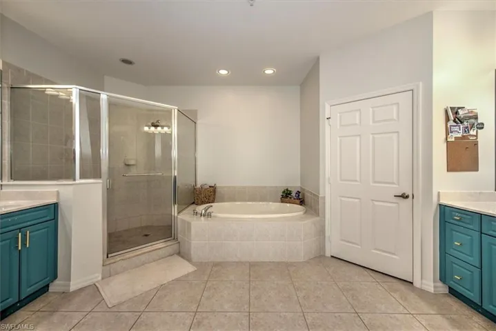 Spacious bathroom featuring an enclosed glass shower, a built-in garden tub with tiled surround, and dual vanity areas with teal cabinetry and light-colored countertops