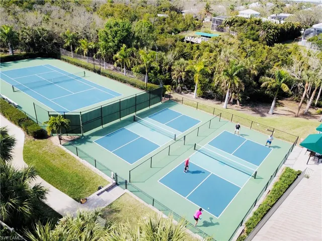 Tennis court and multiple pickleball courts featuring perimeter fencing, manicured landscaping, and mature palm trees