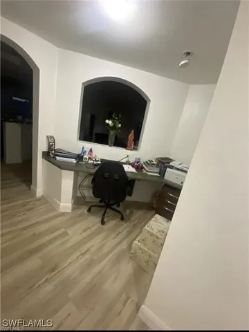 Home office featuring arched walkways, light wood finished floors, and built in study area