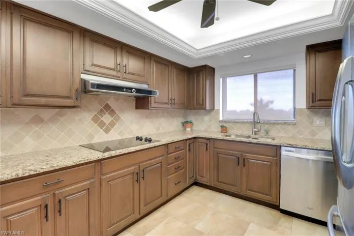 Kitchen featuring appliances with stainless steel finishes, a sink, under cabinet range hood, tasteful backsplash, and light stone counters