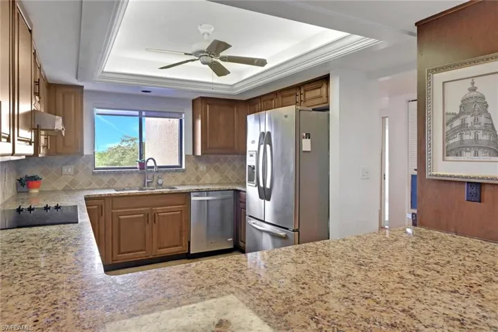 Kitchen featuring appliances with stainless steel finishes, a sink, a raised ceiling, and a ceiling fan